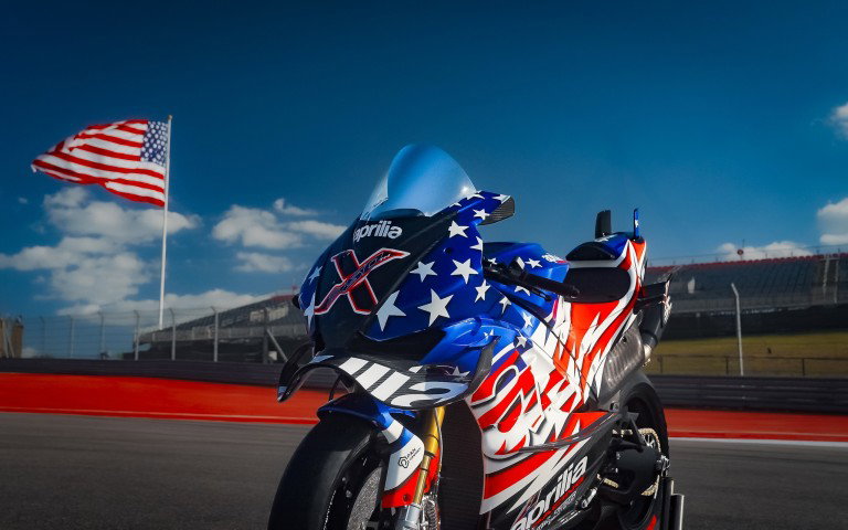 Aprilia X 250TH aus dramatischer Frontperspektive mit US-Flagge im Hintergrund auf dem Circuit of the Americas – Stars-and-Stripes-Sonderedition 2026