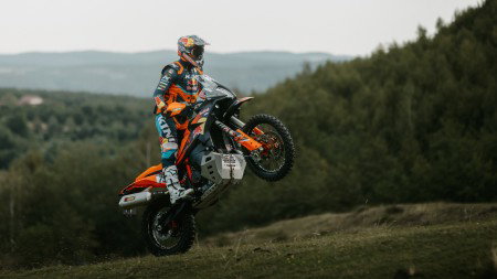 KTM 890 Adventure R Rally 2026 beim Wheelie auf Grashügel mit Bergpanorama – Seitenansicht rechts
