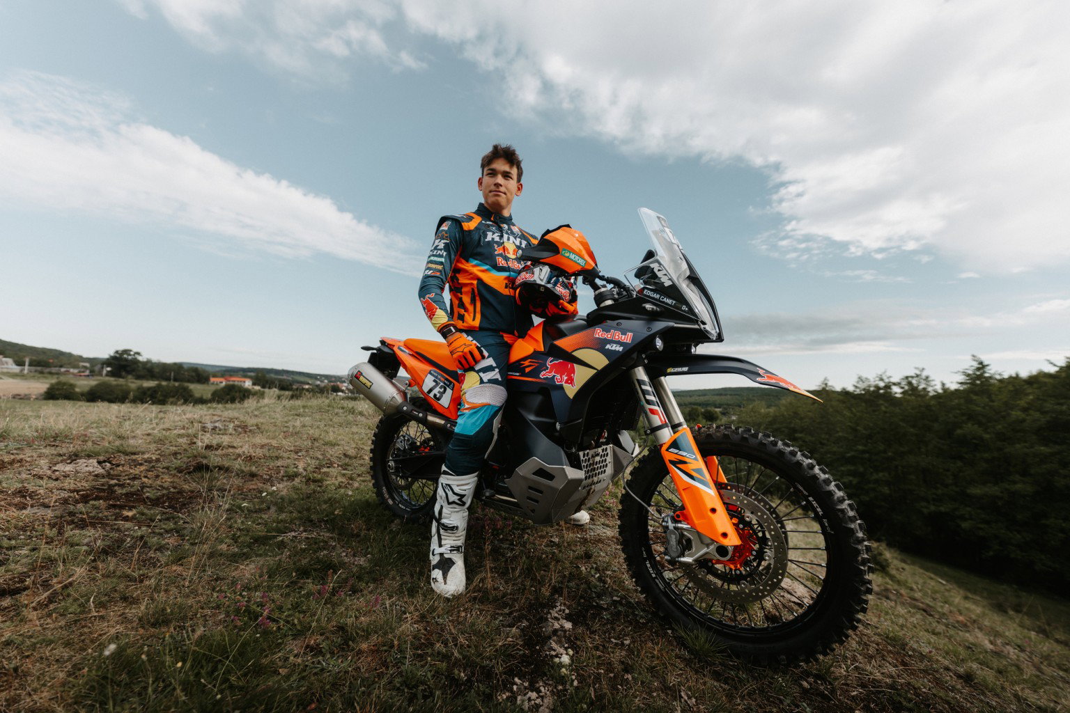 Fahrer steht neben KTM 890 Adventure R Rally 2026 im Gelaende – Outdoor Portrait mit Wolken