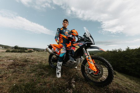KTM 890 Adventure R Rally 2026: Limited Special Model with Dakar DNA Available at Dealers from April Fahrer steht neben KTM 890 Adventure R Rally 2026 im Gelaende – Outdoor Portrait mit Wolken