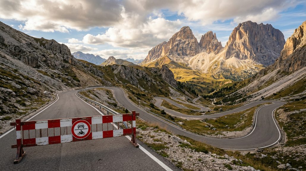 Grödner Joch Passstraße in den Dolomiten mit rot-weißer Absperrschranke und Durchfahrtsverbotsschild, kurvige Serpentinen vor dramatischer Felsenkulisse der Sella-Gruppe im Abendlicht