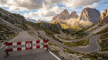 Grödner Joch Passstraße in den Dolomiten mit rot-weißer Absperrschranke und Durchfahrtsverbotsschild, kurvige Serpentinen vor dramatischer Felsenkulisse der Sella-Gruppe im Abendlicht