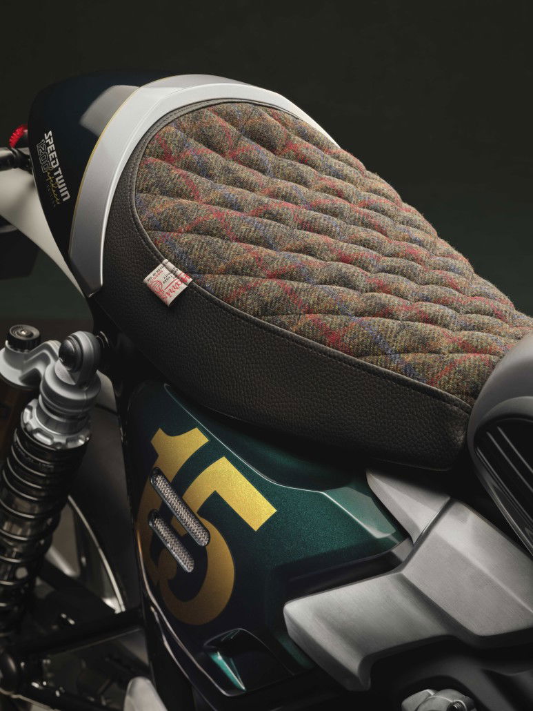 Triumph Speed Twin 1200 Cafe Racer DGR Edition: One-Off With Harris Tweed for a Good Cause 1 Triumph Speed Twin 1200 Cafe Racer DGR Edition 2026 – Nahaufnahme der Harris-Tweed-Bullet-Sitzbank mit Rautensteppung, Harris-Tweed-Authority-Label und 15-Jubiläumsgrafik auf Competition-Green-Seitenverkleidung