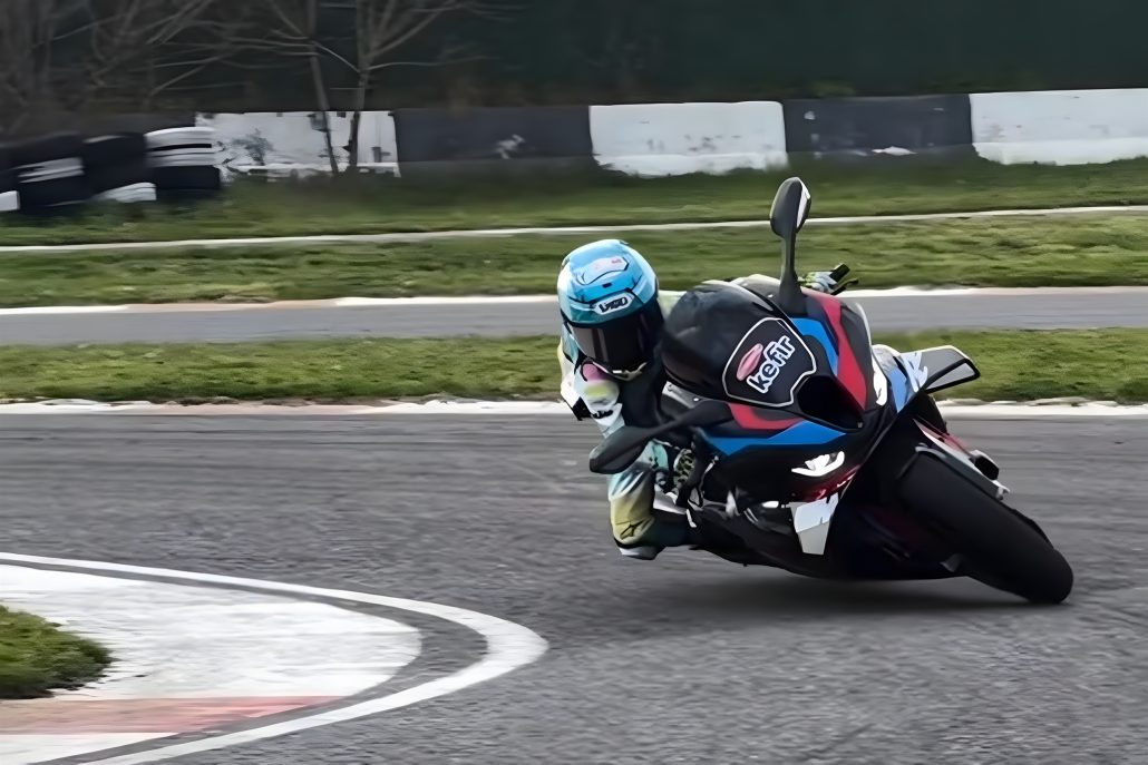 Zayn Sofuoglu in Schräglage auf der BMW M 1000 RR auf einer Rennstrecke, türkisfarbener Kombi mit Kefir-Sponsor, BMW M-Farben am Heck