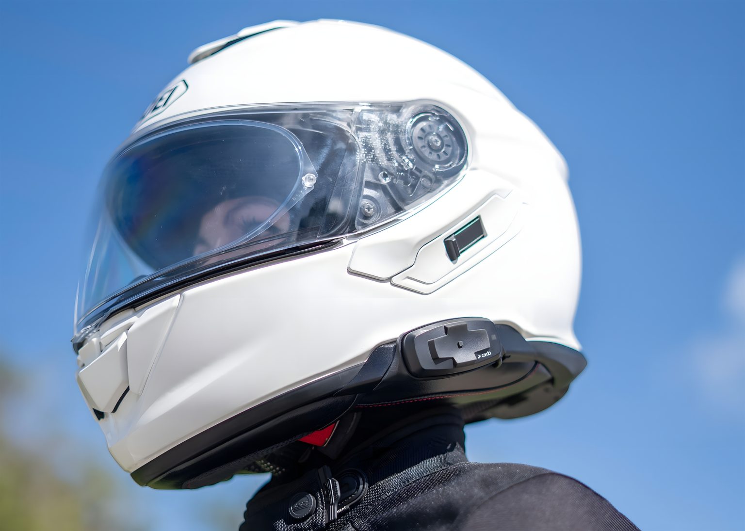 Cardo Packtalk-S and 4X-S for Shoei GT-Air 3, NEOTEC 3, and J-Cruise 3 Cardo Packtalk-S für Shoei – Seitenansicht am weißen Shoei-Helm mit sichtbarem Steuermodul am Kinnbereich, blauer Himmel im Hintergrund