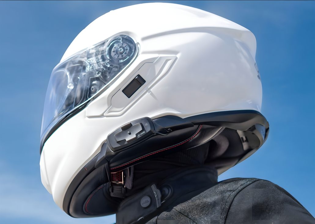 Cardo Packtalk-S and 4X-S for Shoei GT-Air 3, NEOTEC 3, and J-Cruise 3 3 Cardo Packtalk-S for Shoei – close-up of integration on white Shoei helmet with battery and control module at chin strap, blue sky