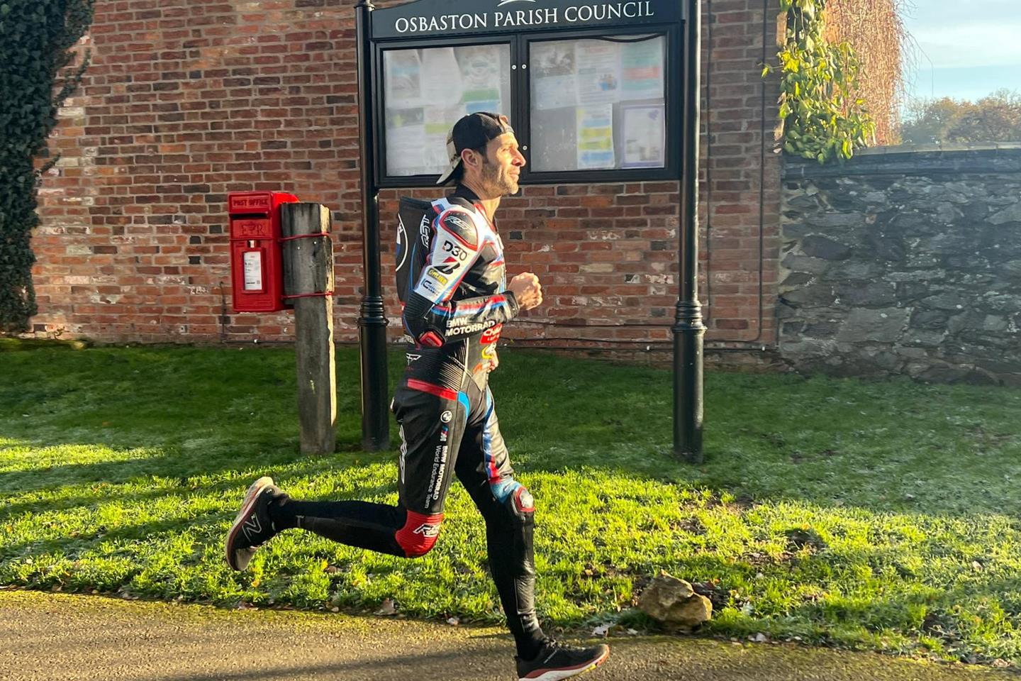 Sylvain Guintoli training run in BMW Motorrad RST racing leather suit on a village road in Osbaston, England, with red post box and brick wall