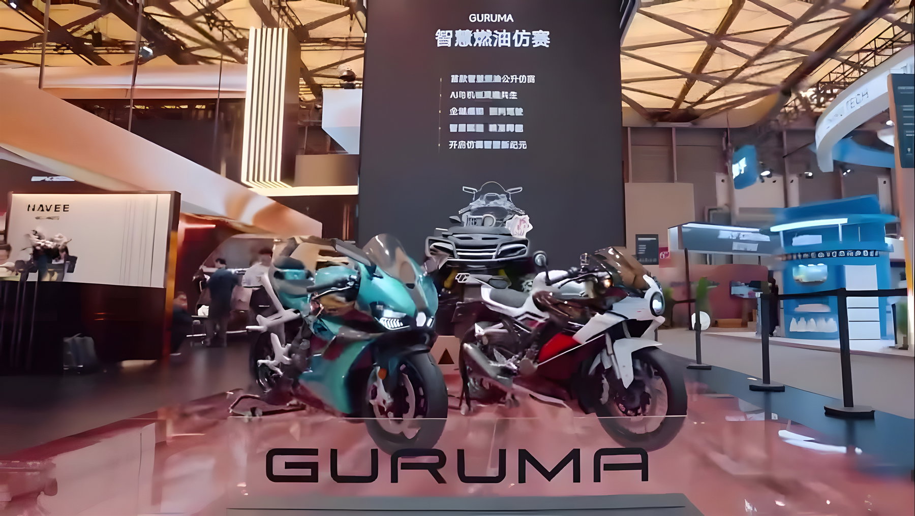 Guruma 1000 RR – Messestand-Übersicht mit türkisem und weiß-rotem Modell vor Guruma-Werbewand