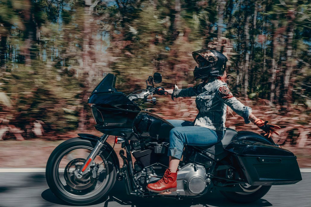 Harley-Davidson RIDE Markenplattform – Fahrerin auf schwarzer Road Glide in dynamischer Fahrt auf Waldstraße mit Bewegungsunschärfe im herbstlichen Hintergrund