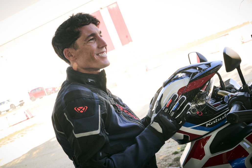 Honda x IXON Collection 2027 – Smiling rider in dark blue IXON Odin Adventure jacket with Kabuto helmet in Honda colors on a Honda Africa Twin