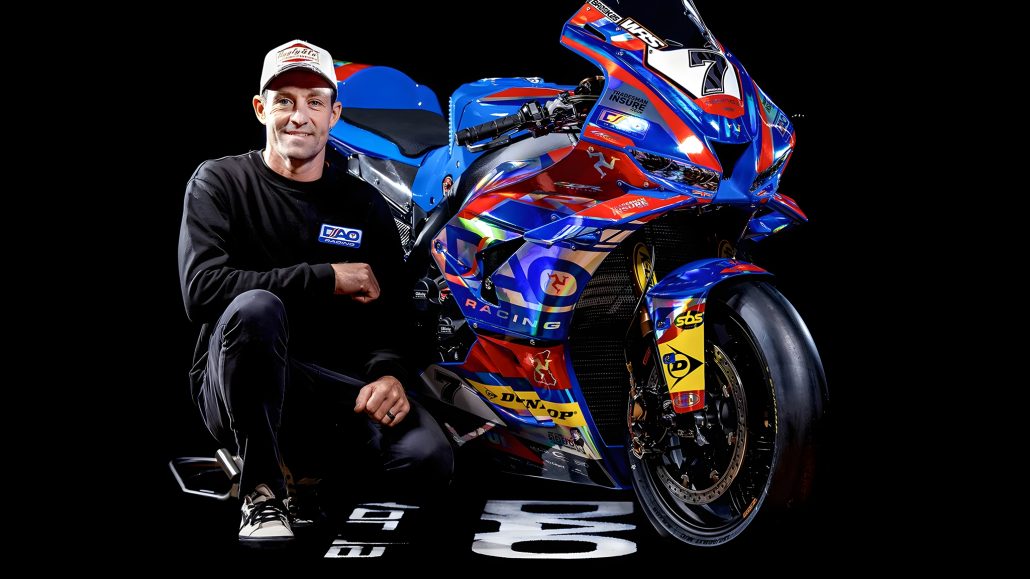 Josh Brookes posiert vor seiner DAO Racing Ducati Panigale im Studio – Fahrer in schwarzem DAO-Sweater mit geballter Faust neben dem Superbike in blau-rot-orangener Lackierung