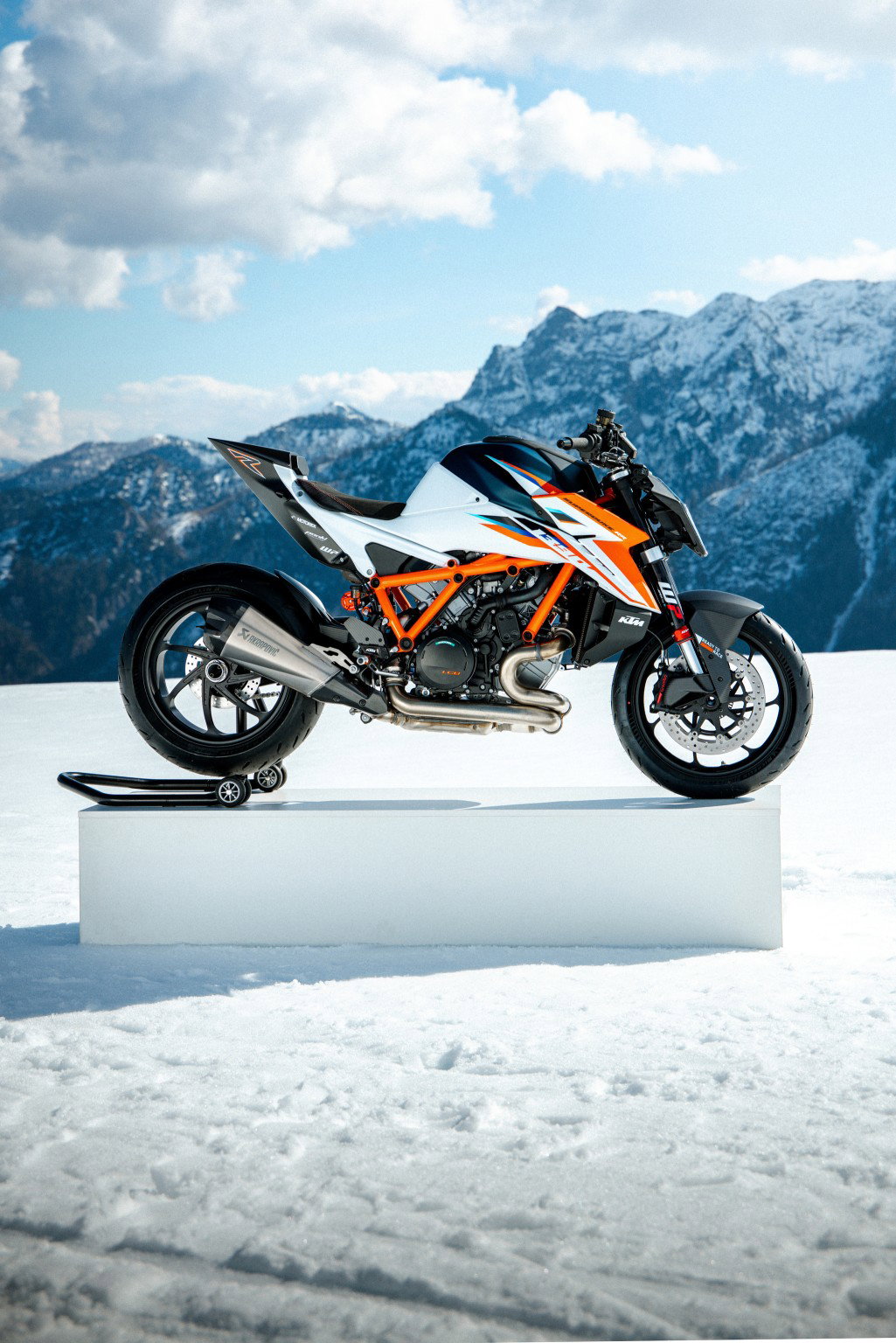 KTM 1390 Super Duke RR 2026 – Seitenansicht in Weiß-Orange auf Podest vor Alpenpanorama im Schnee