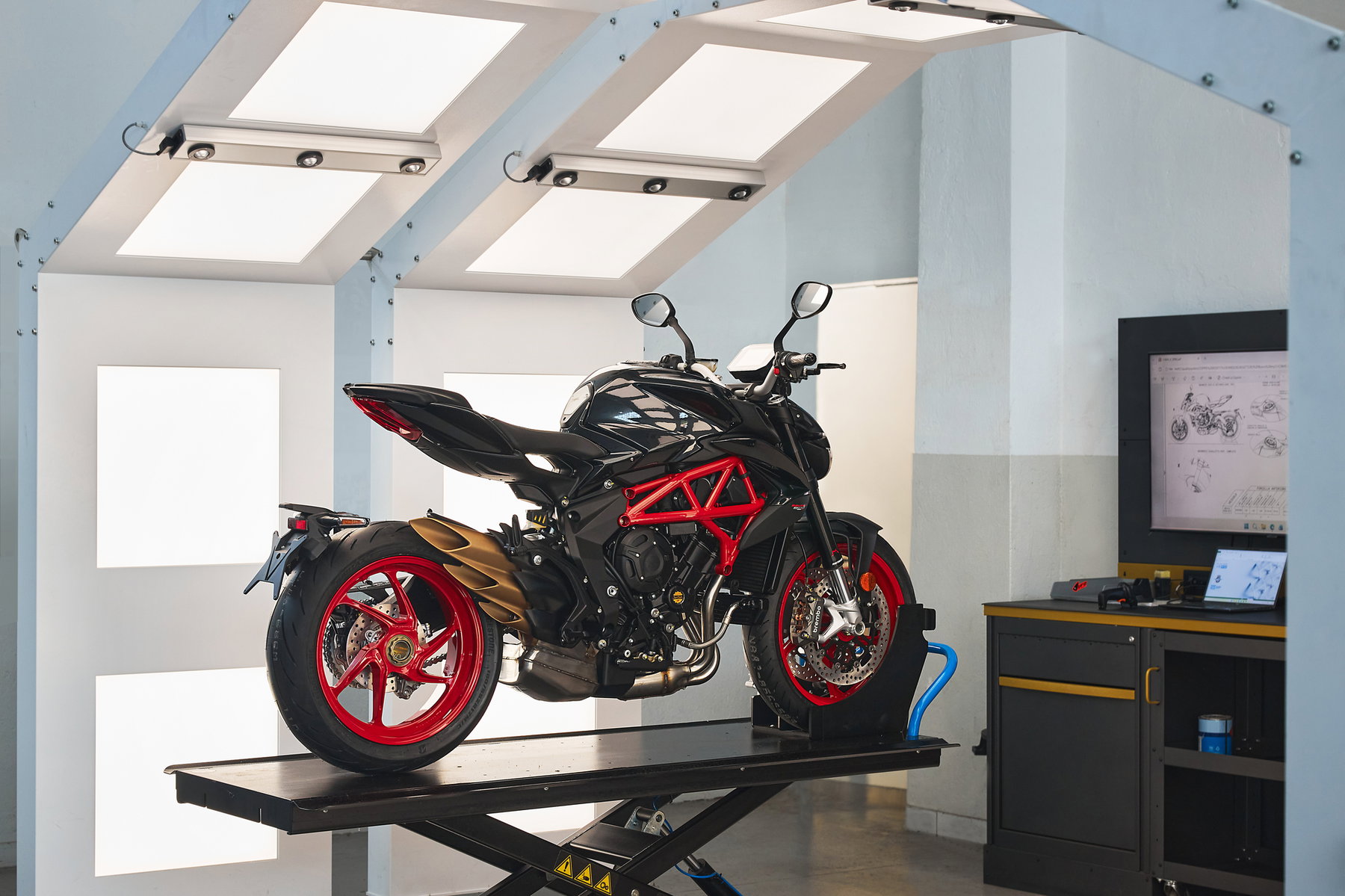 MV Agusta Brutale 800 Nero Carbonio 2026 – Heckansicht schräg links mit Dreifach-Auspuffanlage, goldener Einarmschwinge, roten Felgen und durchsichtigem Unterbau-Design im Studio
