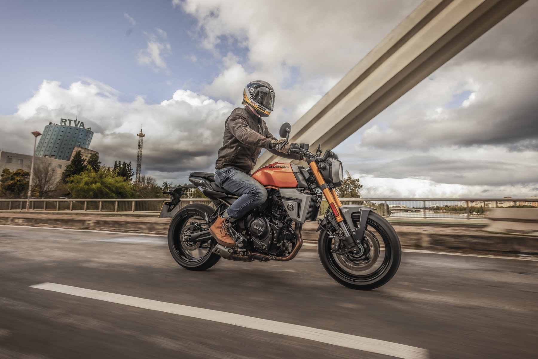 Suzuki Deutschland senkt Preise und will Marktanteil verdreifachen 3 Suzuki GSX-8T 2026 – Neo-Retro-Streetbike in Fahrt auf einer Brücke, kupfer-orangefarbene Lackierung mit 776-ccm-Parallel-Twin-Motor, Fahrer in lässiger Motorradkleidung bei bewölktem Himmel