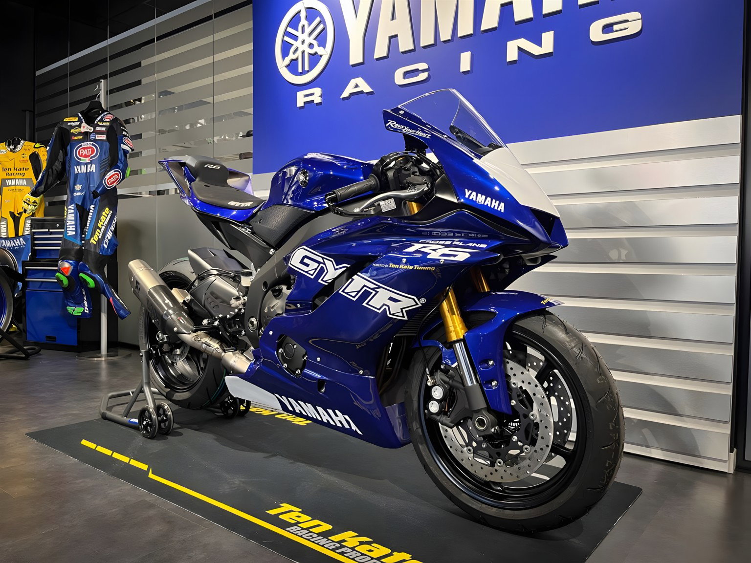 Yamaha R6 Crossplane Ten Kate – Dreiviertelansicht vorne rechts im Showroom mit goldenen Öhlins-Gabeln