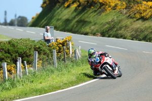 Fahrer auf rot-weisser Honda in Schraglage mit Zuschauer am Streckenrand – Isle of Man TT 2026 Free Practice