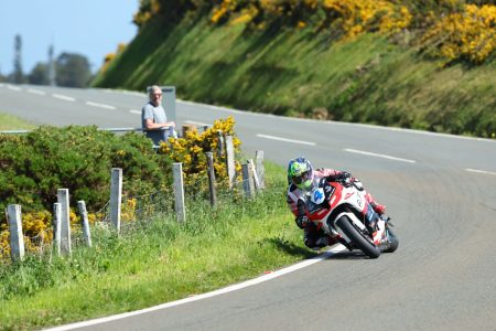 Fahrer auf rot-weisser Honda in Schraglage mit Zuschauer am Streckenrand – Isle of Man TT 2026 Free Practice