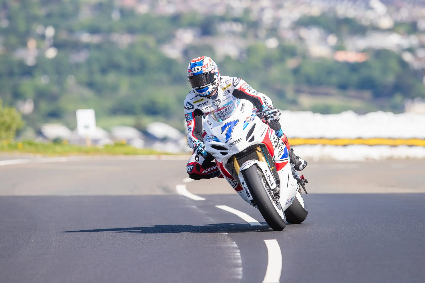Startnummer 7 auf weiss-rot-blauem Superbike in Schräglage mit Douglas im Hintergrund – Isle of Man TT 2026 Free Practice