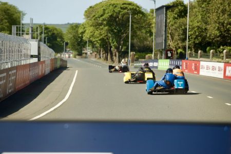 Mehrere Sidecar-Gespanne auf der Glencrutchery Road nach dem Start – Isle of Man TT 2026 Newcomers Speed Controlled Lap blaues und gelbes Gespann Motul-Werbung