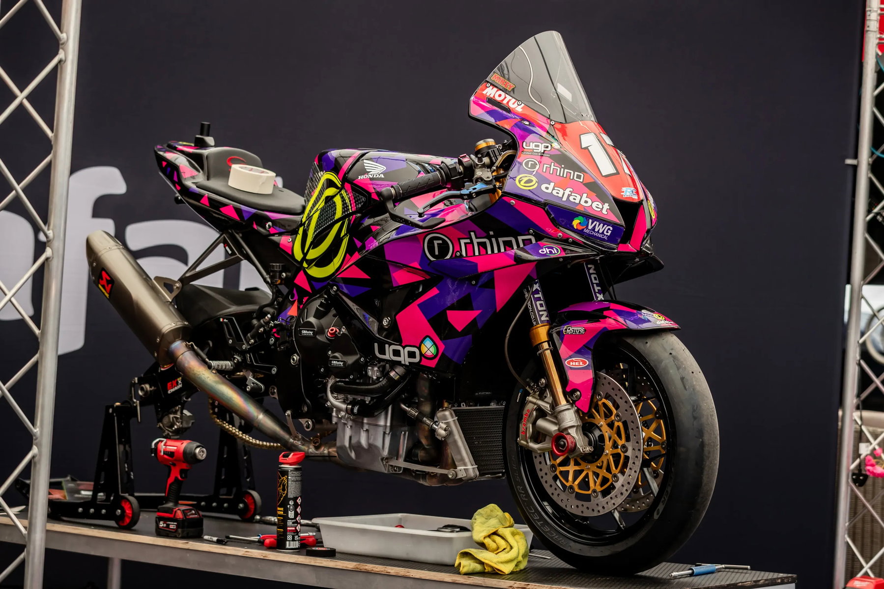 TT 2026: Harrison fährt Wochenbestzeit vor dem ersten Rennen 6 Superbike mit Startnummer 1 in pink-violetter Lackierung mit Rhino und Dafabet Sponsoring auf Montagestaender – Isle of Man TT 2026 Paddock