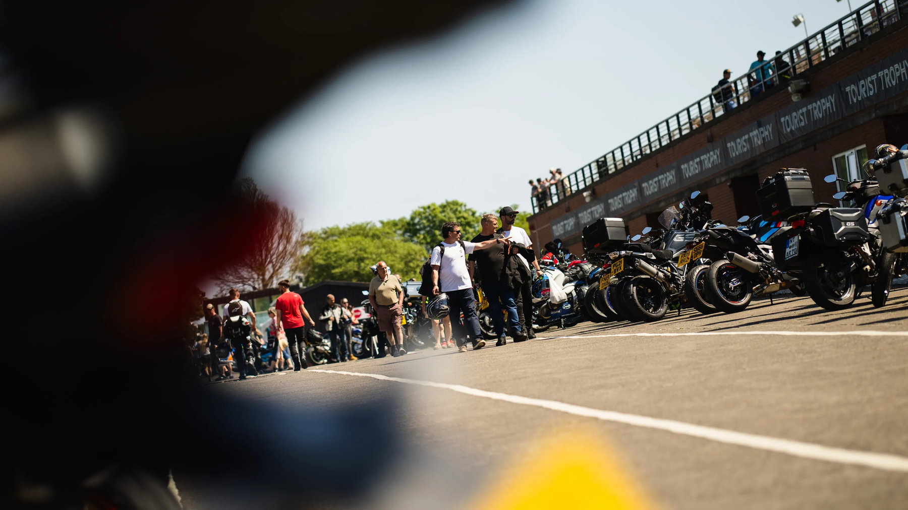 TT 2027: Warum die 100. Senior TT nicht mehr das Finale ist 1 Blick durch Motorräder auf Fans und die Tourist-Trophy-Tribüne im Paddock – Isle of Man TT 2026