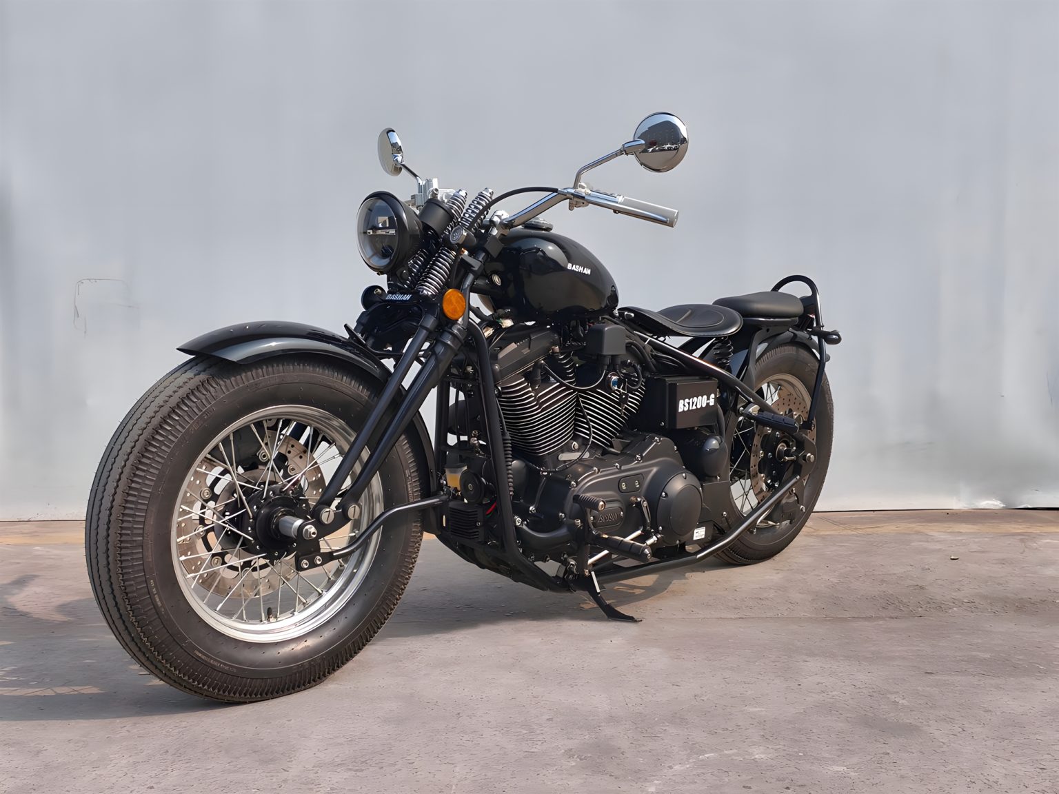 Bashan BS1200-G 2027 – Seitenansicht von schräg vorne links, Gesamtansicht des schwarzen Hardtail-Bobbers vor Betonwand
