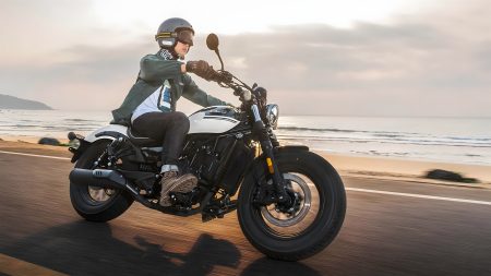 CFMoto CL-C250 Cruiser in Fahrt auf einer Küstenstraße – Fahrer mit Jethelm auf dem schwarz-weißen Einzylinder-Cruiser bei Sonnenuntergang am Strand