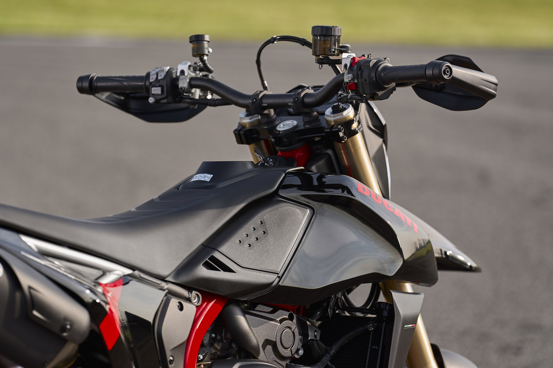 Ducati Hypermotard 698 Mono Nera 2027 – Cockpit-Detailansicht mit schwarzem Tank, Ducati-Schriftzug in Rot, Marzocchi-USD-Gabel und Handprotektoren auf Rennstrecke