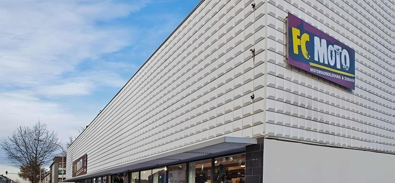 FC-Moto Filiale Würselen Außenansicht – Großes Geschäftsgebäude mit weißer Fassade und buntem FC-Moto-Logo, Aufschrift Motorradbekleidung und Zubehör