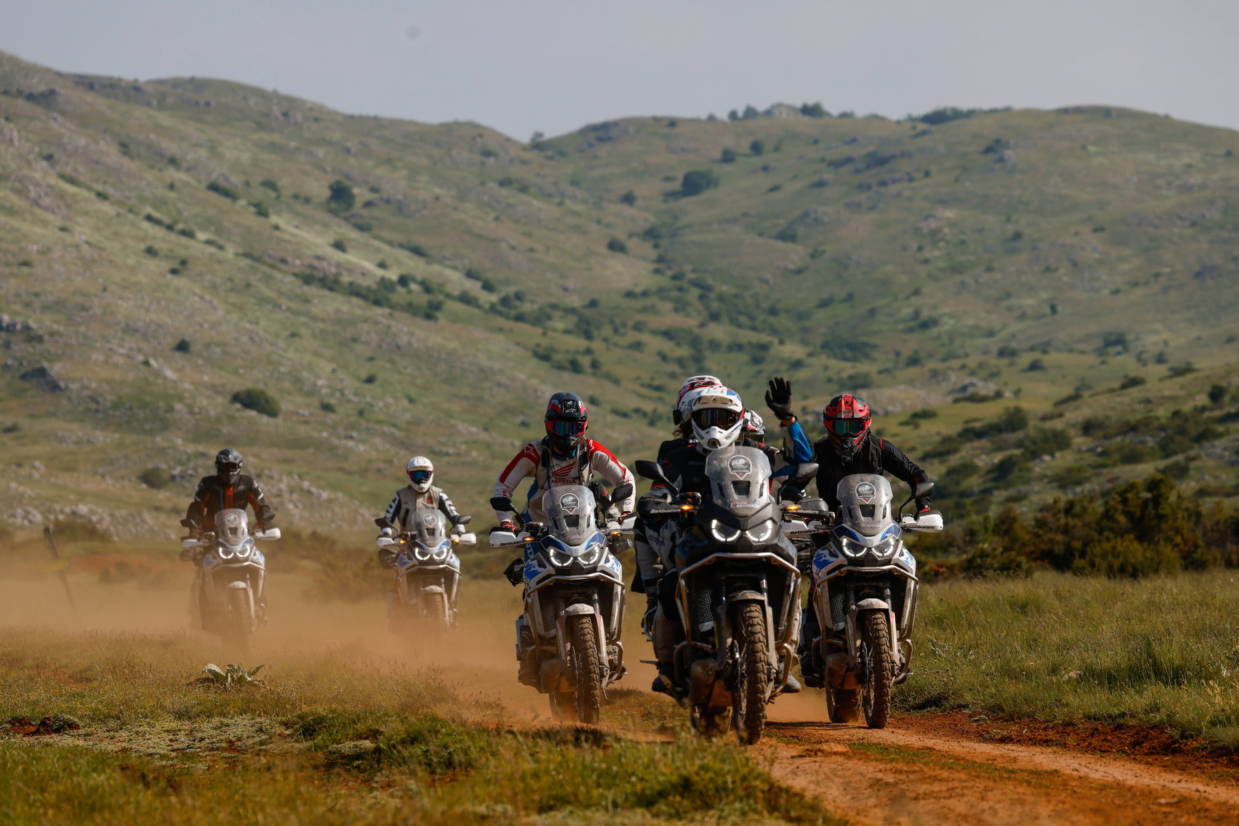 Honda Adventure Roads – Gruppe von Africa-Twin-Fahrern auf staubiger Offroad-Piste durch grüne Hügellandschaft
