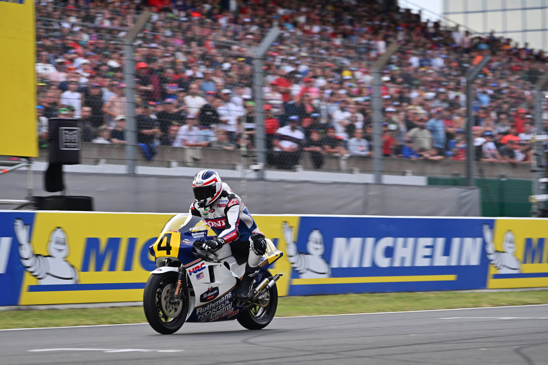 Honda CB1000F: Freddie Spencer und historische Rennmaschinen begleiten das neue Naked Bike 4 Honda CB1000F 2026 – Honda NSR500 Rothmans auf der Geraden in Le Mans vor voll besetzter Tribüne und Michelin-Bandenwerbung
