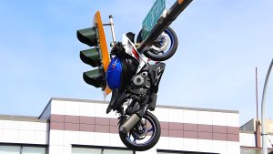 Motorradunfall Delta Kanada – Nahaufnahme eines blauen Sportmotorrads kopfüber an einer Ampel hängend, verkeilt im Mall-Entrance-Schild, blauer Tank und Motor sichtbar, Geschäftsgebäude im Hintergrund