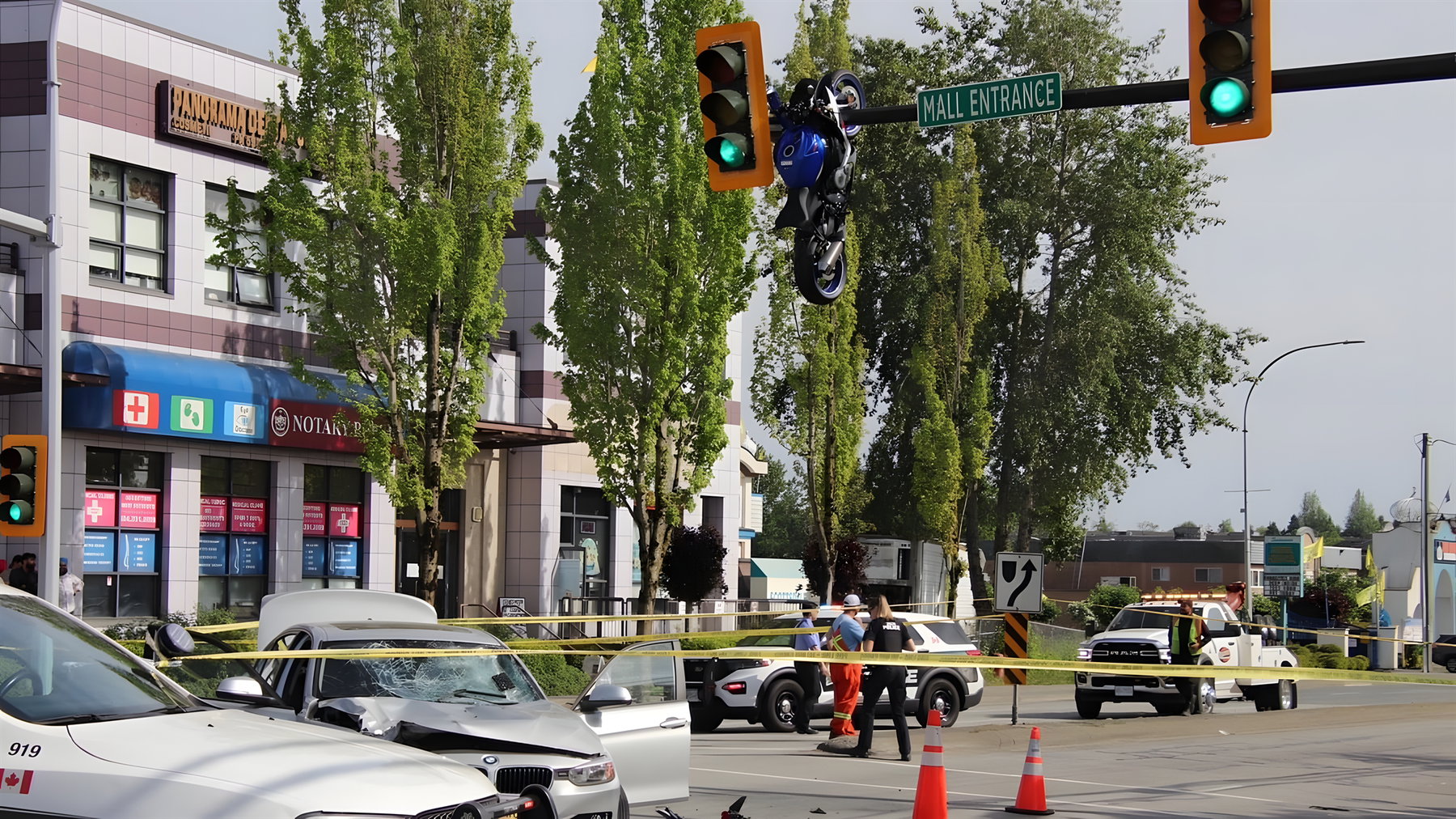 Motorcycle crash Delta Canada – crash scene at Scott Road intersection, motorcycle hanging from traffic light, white car with shattered windshield behind police tape, emergency vehicles and pylons on scene
