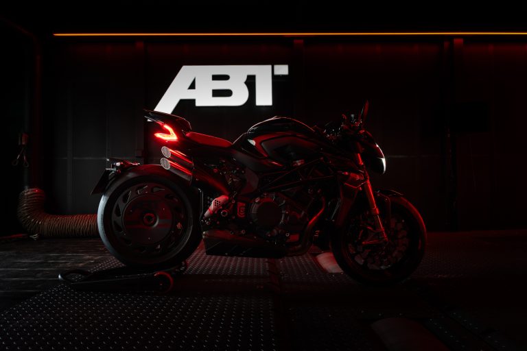 MV Agusta Brutale 1000 ABT 2026 – Atmosphärische Seitenansicht rechts in dunkler Werkstatt-Umgebung mit beleuchtetem ABT-Logo im Hintergrund, rote Ambientebeleuchtung, Carbon-Radabdeckung