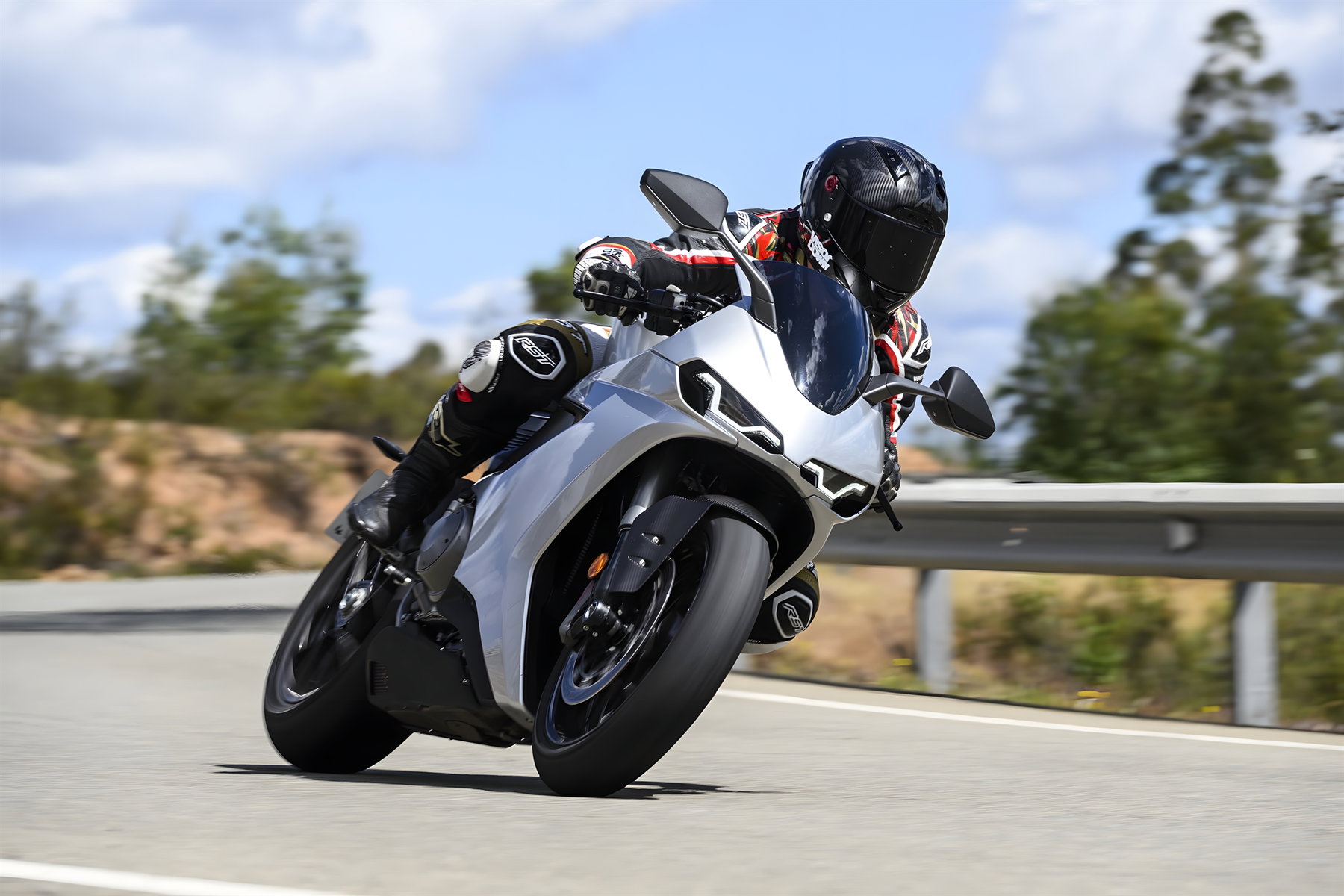 Norton Manx R With Suspension Travel Sensors: What Changes For Riders 1 Norton Manx R Signature 2026 – rider leaning through a bend on an Andalusian country road, front view with crash barrier