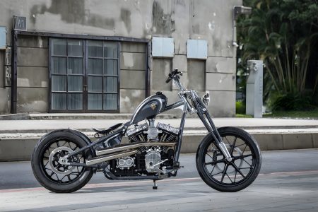 Rough Crafts Aeternum Blade Harley-Davidson Street Bob – Seitenansicht von rechts mit komplettem Chopper-Profil, Nardo Grey Lackierung, polierter Edelstahl-Auspuffanlage und Frisco-Tank vor Industriegebäude