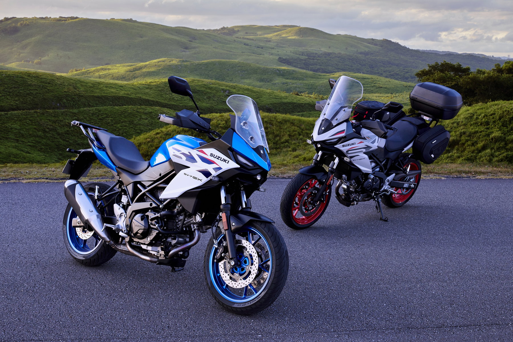 Suzuki SV-7GX 2026 Touring Edition – zwei Modelle in Blau/Weiß und Pearl Matte Greige mit Touring-Zubehör vor Bergpanorama