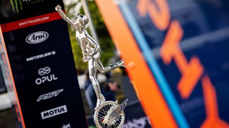 Nahaufnahme der Senior-TT-Trophaee mit Merkur-Statuette auf gefluegeltem Rad zwischen Sponsorentafeln im Fahrerlager - Senior TT, Isle of Man TT 2026