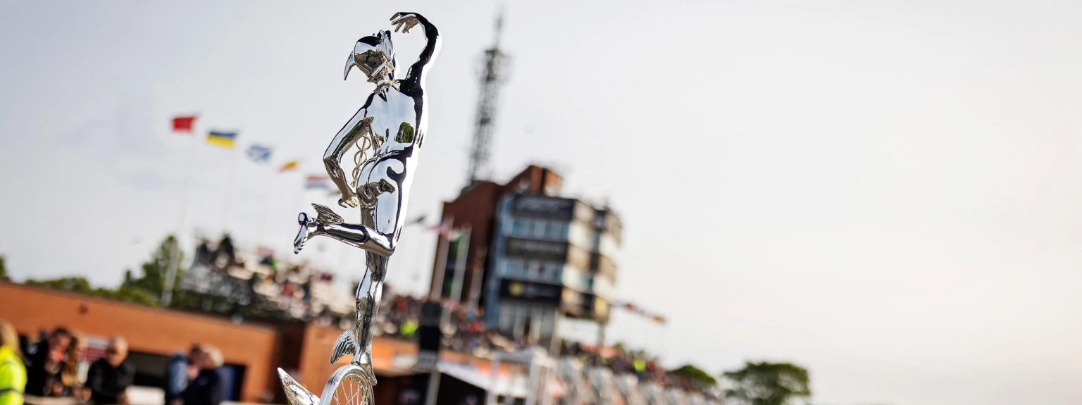 Die silberne Senior-TT-Trophaee mit Merkur-Statuette auf gefluegeltem Rad vor dem Kontrollturm und der Haupttribuene in Douglas - Senior TT, Isle of Man TT 2026