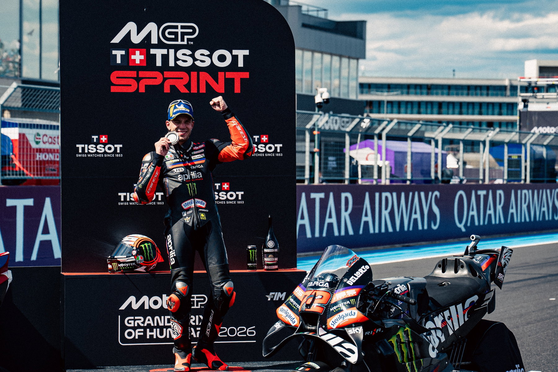 Bezzecchi Suspended After Marshal Incident: Consequences for Championship Lead 4 Marco Bezzecchi feiert mit Medaille neben seiner Aprilia RS-GP26 am Tissot-Sprint-Board – MotoGP Ungarn GP Balaton Park 2026
