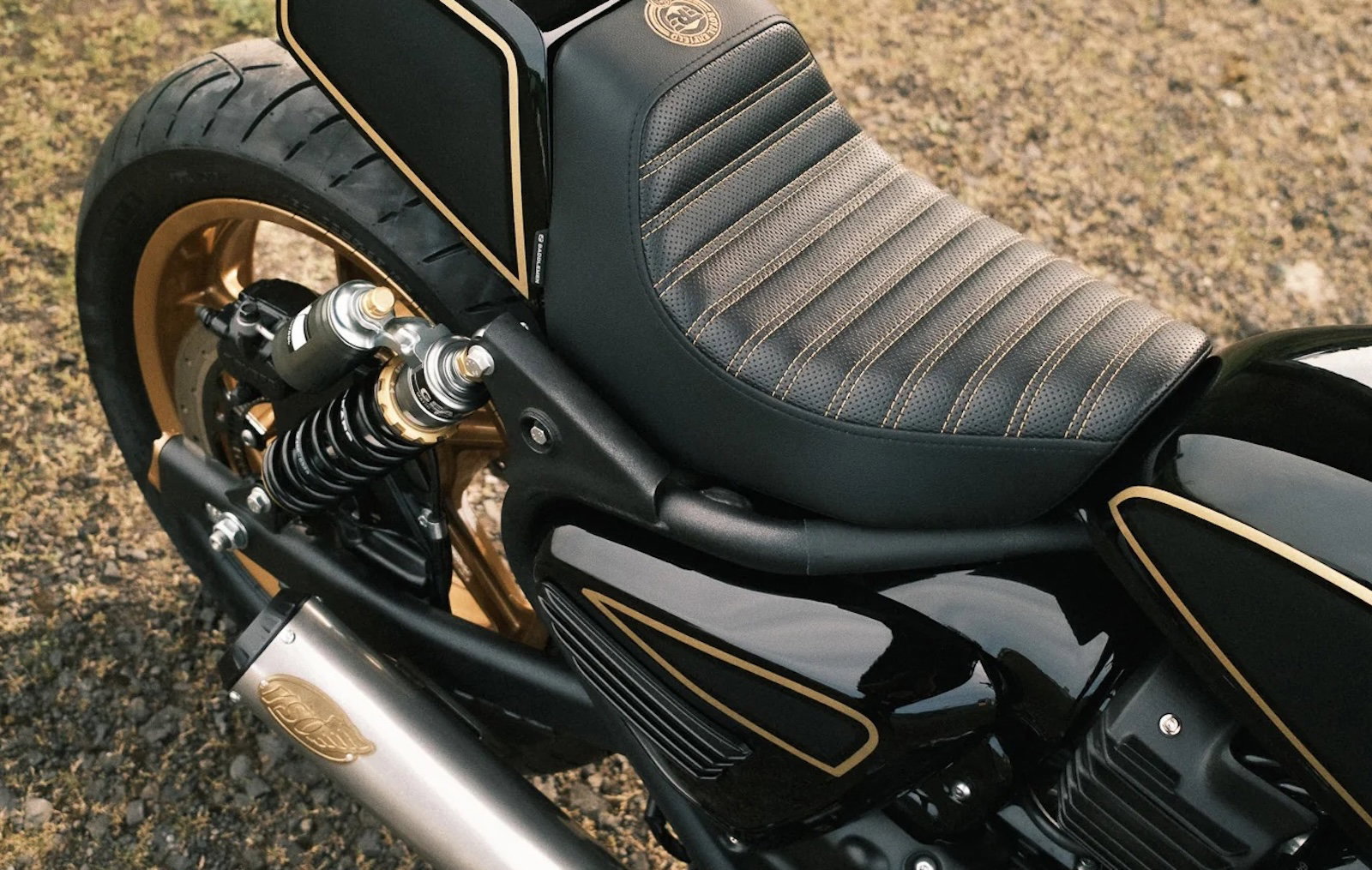 Royal Enfield Reload 650 – seat and tail section from top right with perforated gunfighter solo seat, gold stitching, Öhlins shocks, ribbed side cover with gold trim and S&S exhaust