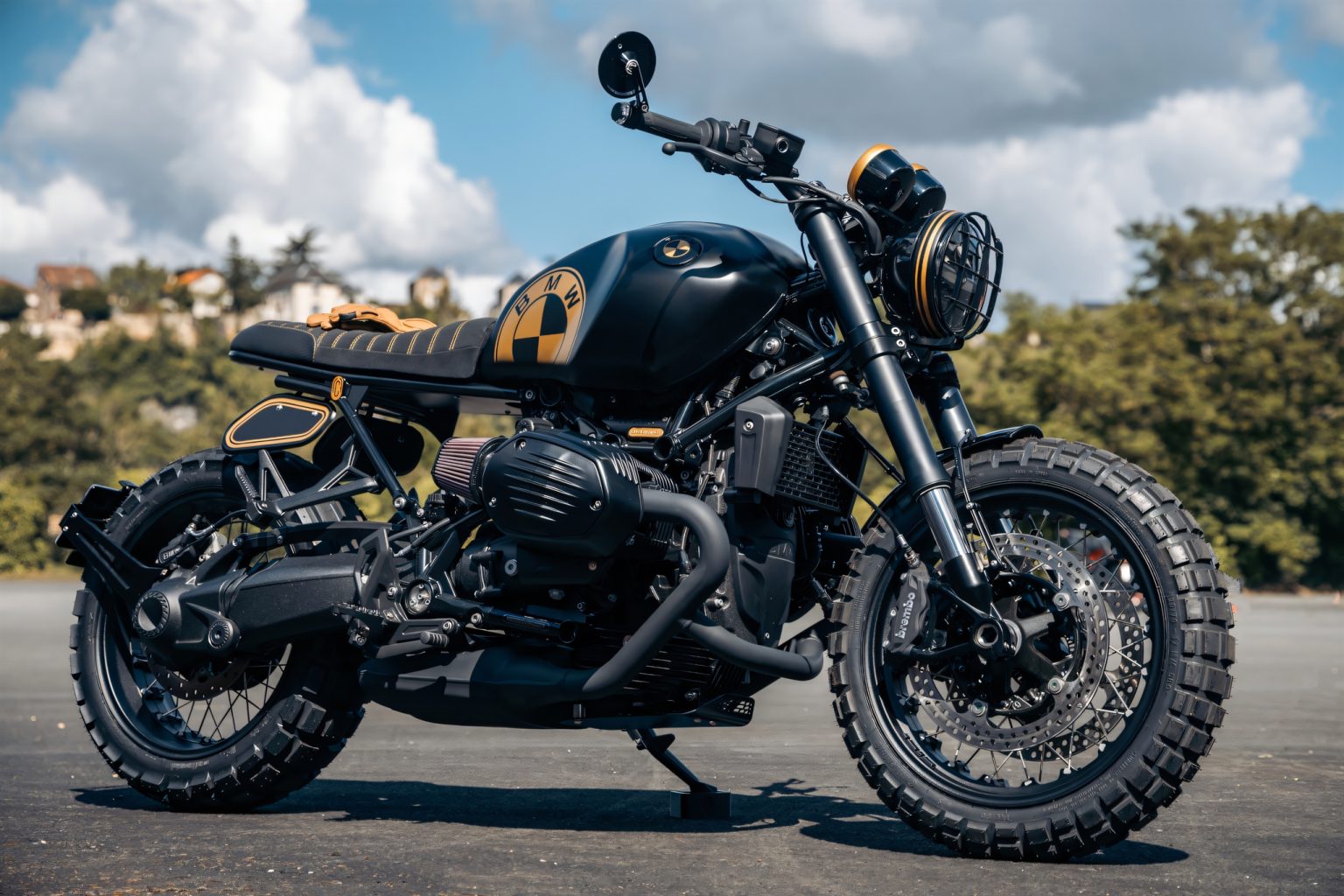 BMW R 12 als Scrambler: FCR Original verwandelt den Cruiser BMW R 12 Scrambler by FCR Original – Rechte Dreiviertel-Frontansicht mit Boxer-Motor, Continental TKC80 Stollenreifen, goldenem Scheinwerferring und Motogadget-Spiegel vor bewölktem Himmel