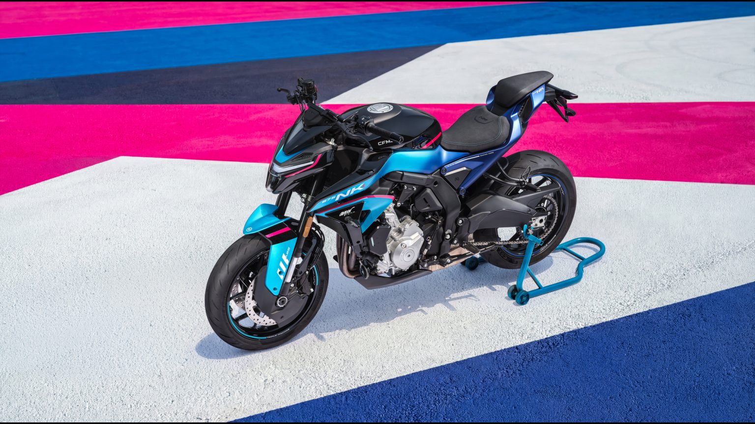 CFMOTO 675NK 2026 in Champion Blue – Seitenansicht von links auf farbenfroher Rennstrecken-Fläche, abgestützt auf blauem Montageständer