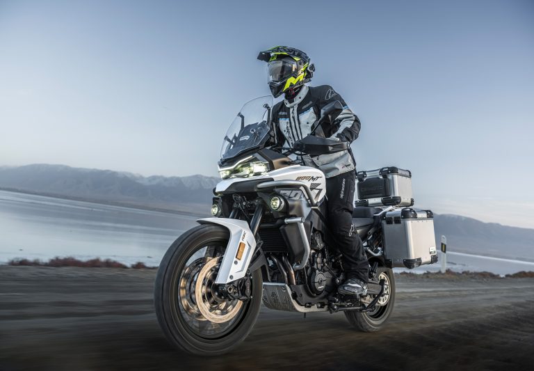 CFMOTO 800MT-ES 2026 in Glacier White – Fahraufnahme mit Fahrer und Aluminium-Seitenkoffern auf der Straße vor Bergkulisse