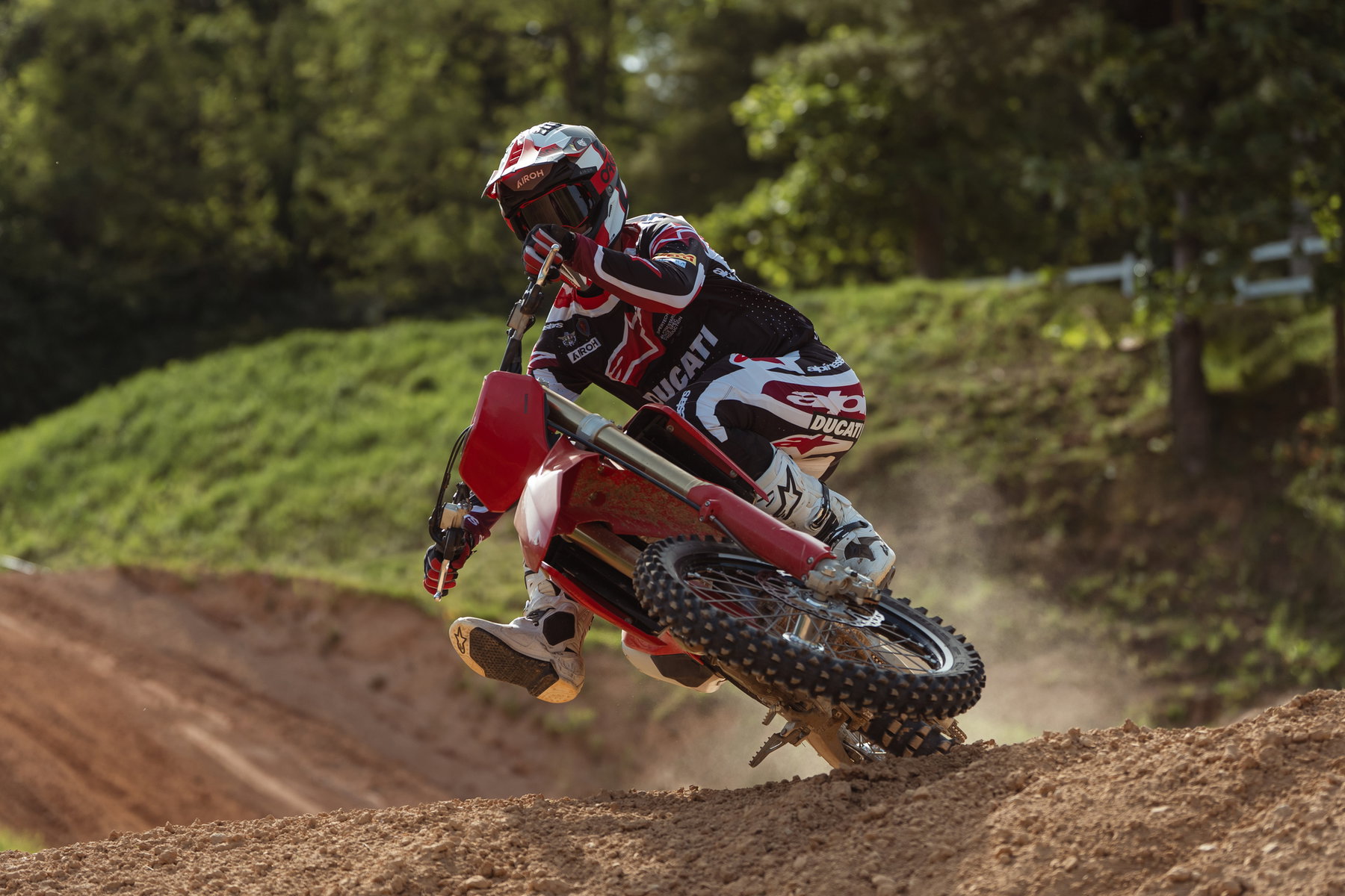 Ducati Desmo250 MX kommt: Desmodromik erobert die 250er-Klasse 7 Ducati Desmo250 MX 2027 – Fahrer in roter Ducati-Alpinestars-Kombi beim Anbremsen einer Anliegerkurve, aufspritzender Sand vor grünem Waldhintergrund