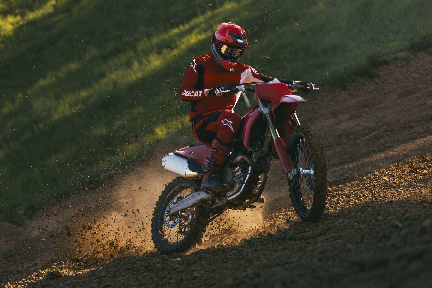 Ducati Desmo250 MX kommt: Desmodromik erobert die 250er-Klasse 6 Ducati Desmo250 MX 2027 – Frontansicht des Fahrers in roter Montur auf sandiger Motocross-Strecke im warmen Abendlicht, Staubfahne hinter dem Hinterrad