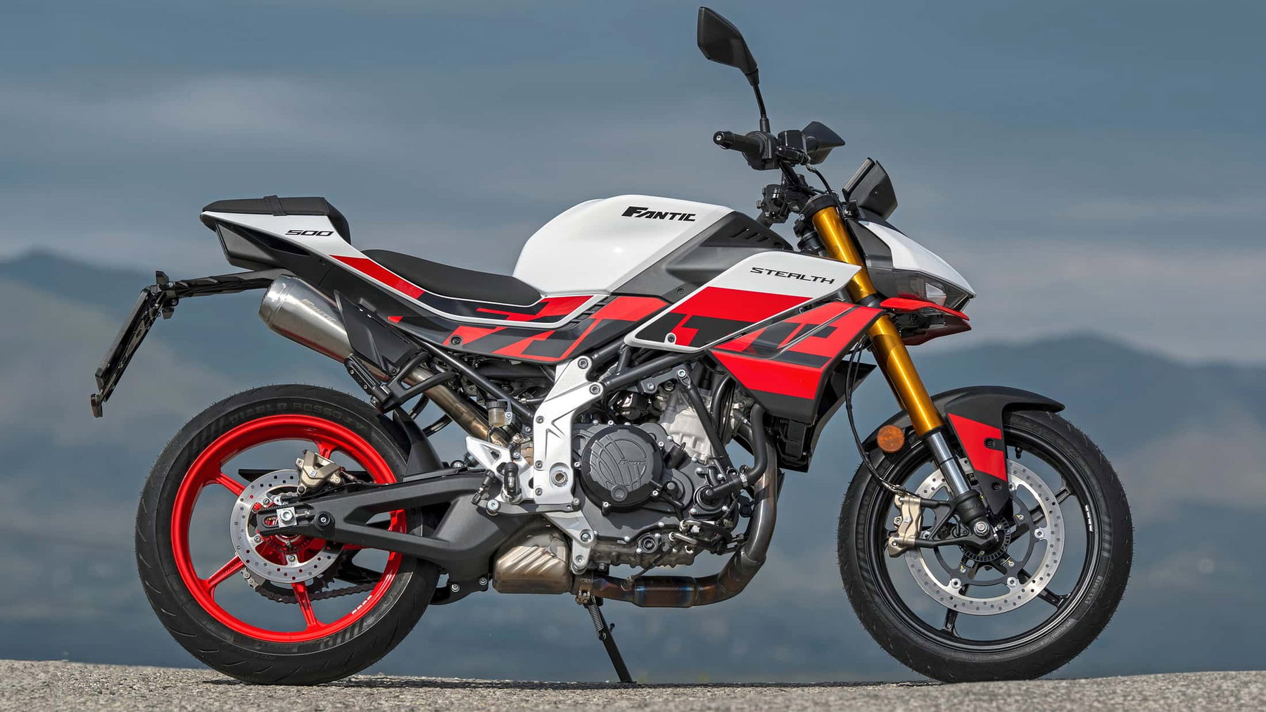 Fantic Stealth 500: 45 hp, 147 kg and Caballero 500 Technology 3 Fantic Stealth 500 2026 – right side view in Racing White on mountain road in the Apennines with red cast wheels and gold USD fork