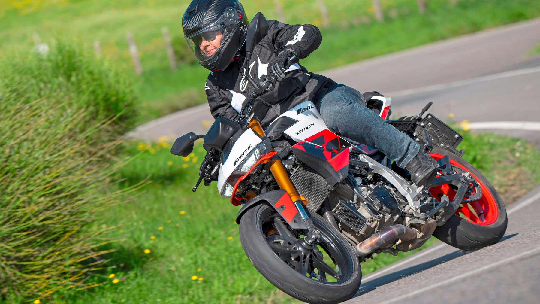 Fantic Stealth 500: 45 hp, 147 kg and Caballero 500 Technology 4 Fantic Stealth 500 2026 – action shot at lean angle on green country road in Racing White with red wheels in the Apennines