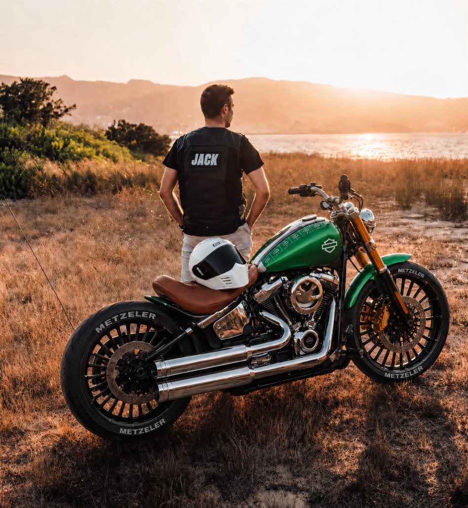 Grüne Harley-Davidson Breakout mit Chrom und braunem Ledersitz – seitliche Ansicht in Abendstimmung an der Küste, Content-Creator Jack NBC steht dahinter
