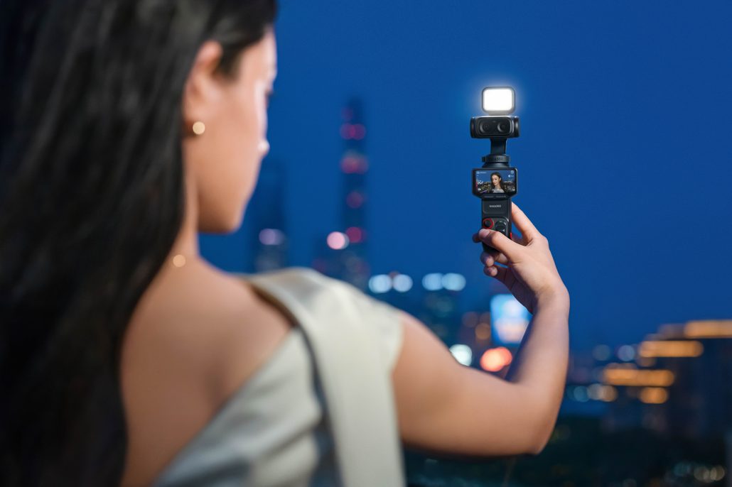 Frau hält die Insta360 Luna Ultra in Nacht Schwarz mit aufgesetztem LED-Licht hoch, im Hintergrund eine beleuchtete Skyline bei Nacht